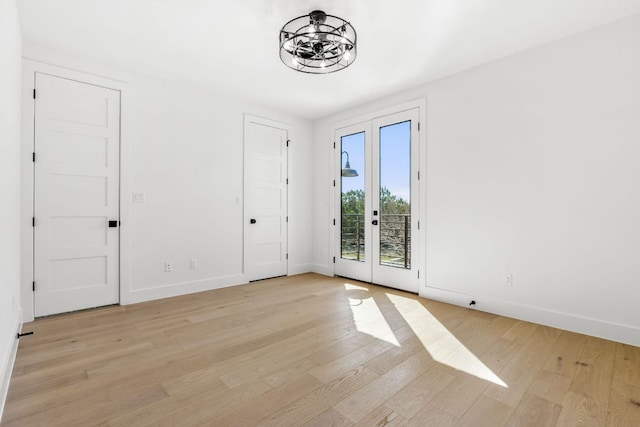 empty room featuring french doors, baseboards, light wood-style flooring, and a chandelier