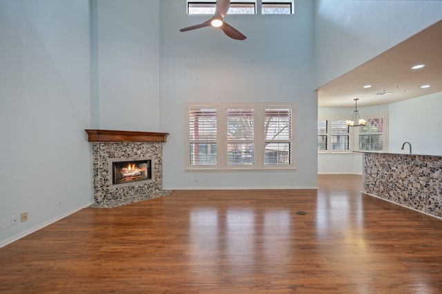 living area with a high ceiling, wood finished floors, a fireplace, and ceiling fan with notable chandelier