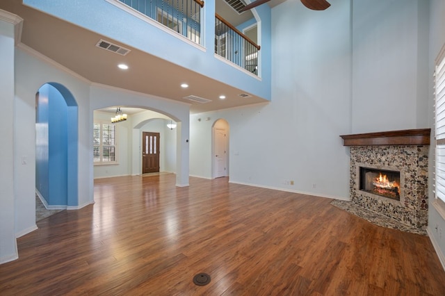 unfurnished living room with visible vents, wood finished floors, arched walkways, a fireplace, and baseboards