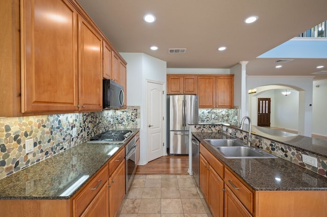 kitchen with brown cabinetry, visible vents, arched walkways, a sink, and appliances with stainless steel finishes