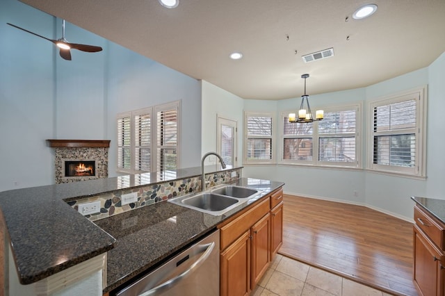 kitchen featuring visible vents, dishwasher, ceiling fan with notable chandelier, brown cabinetry, and a sink