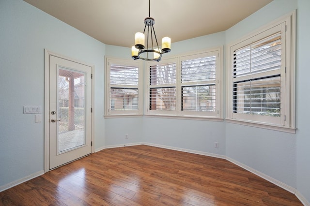 unfurnished dining area with baseboards, a notable chandelier, and wood finished floors