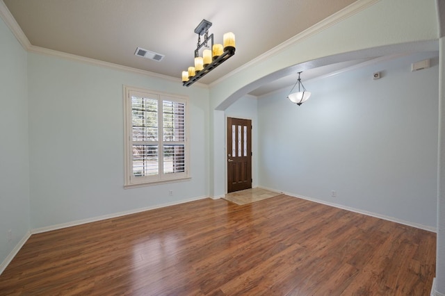 spare room featuring visible vents, wood finished floors, arched walkways, crown molding, and baseboards