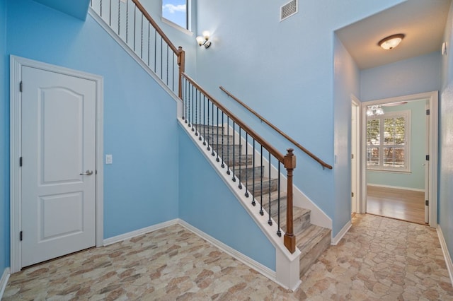 staircase featuring stone finish floor, baseboards, visible vents, and a towering ceiling