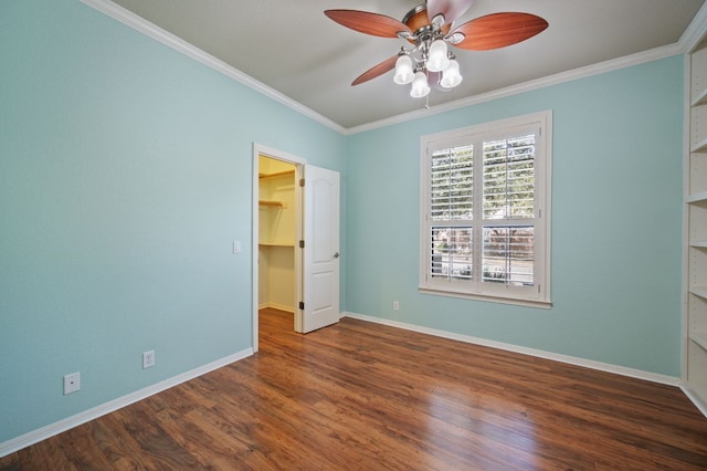 unfurnished bedroom featuring crown molding, a spacious closet, wood finished floors, and baseboards