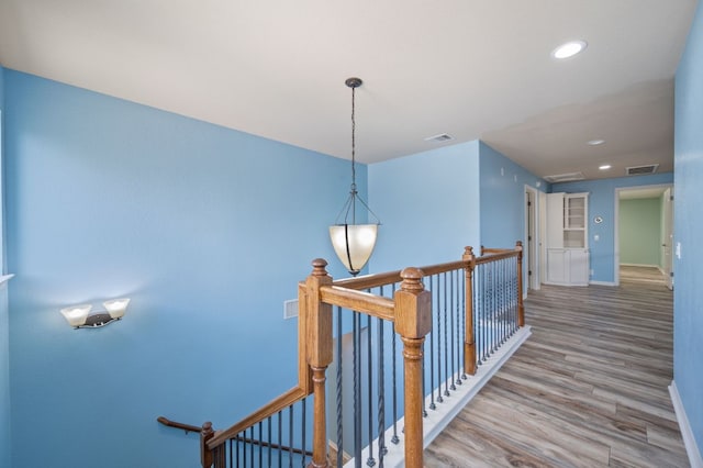 hall with recessed lighting, visible vents, an upstairs landing, and wood finished floors