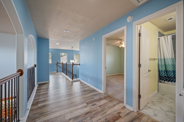 corridor featuring visible vents, an upstairs landing, a textured ceiling, wood finished floors, and baseboards