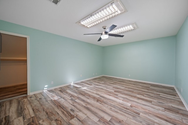 unfurnished bedroom featuring a walk in closet, wood finished floors, baseboards, and ceiling fan