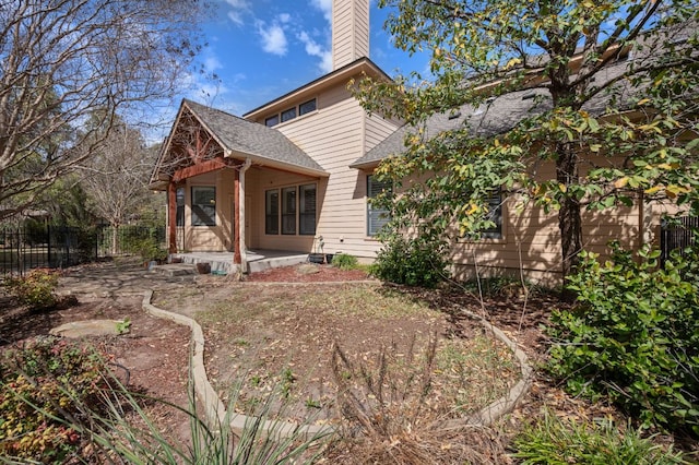 back of house featuring a porch, fence, a chimney, and a shingled roof