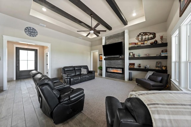 living area with a raised ceiling, a large fireplace, visible vents, and beam ceiling