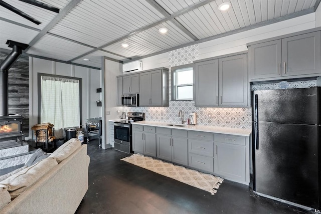 kitchen with gray cabinetry, light countertops, appliances with stainless steel finishes, a wood stove, and a wall mounted AC