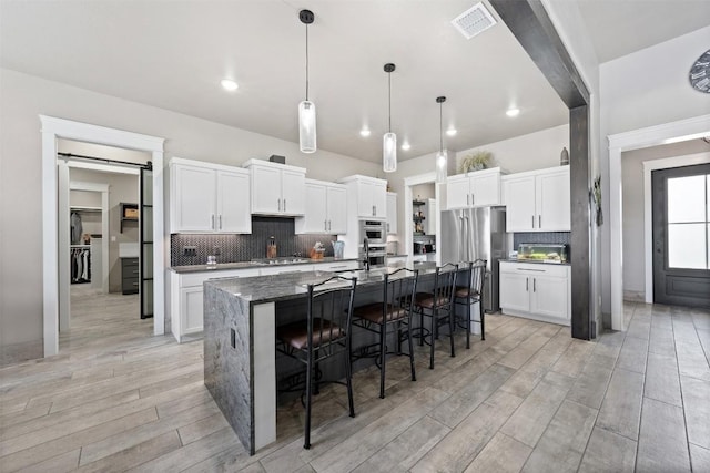 kitchen with visible vents, light wood finished floors, freestanding refrigerator, white cabinetry, and a kitchen breakfast bar