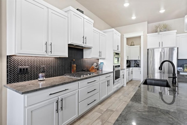 kitchen featuring a sink, wood finish floors, appliances with stainless steel finishes, and dark stone countertops