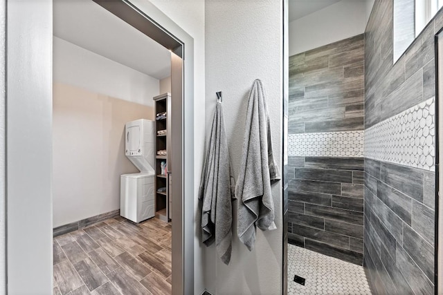 bathroom with wood finished floors, baseboards, stacked washer / drying machine, and walk in shower