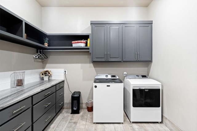 laundry area featuring washing machine and dryer, cabinet space, light wood-type flooring, and baseboards