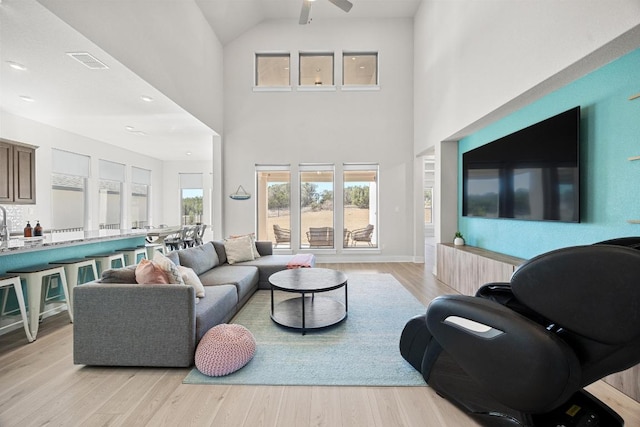 living room with visible vents, ceiling fan, a high ceiling, and light wood-style floors