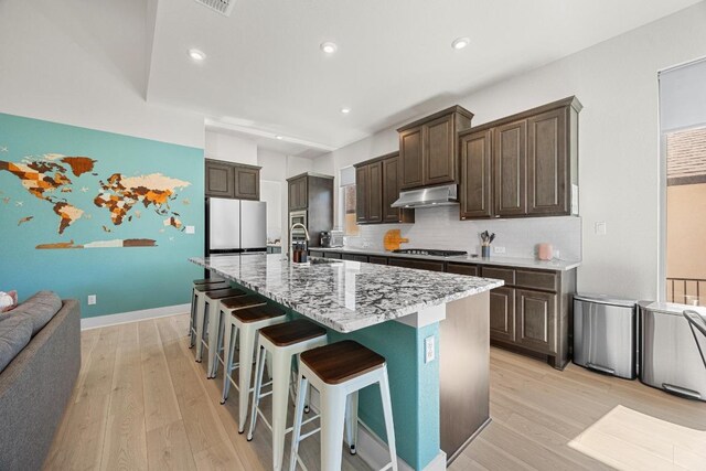 kitchen featuring under cabinet range hood, light wood-type flooring, dark brown cabinetry, and freestanding refrigerator