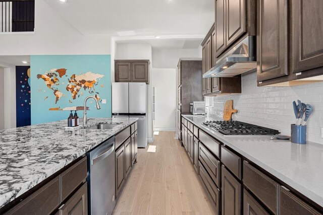 kitchen with light wood-style flooring, a sink, dark brown cabinetry, under cabinet range hood, and appliances with stainless steel finishes