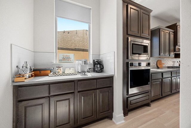 kitchen featuring light wood-style flooring, tasteful backsplash, stainless steel appliances, light countertops, and dark brown cabinets