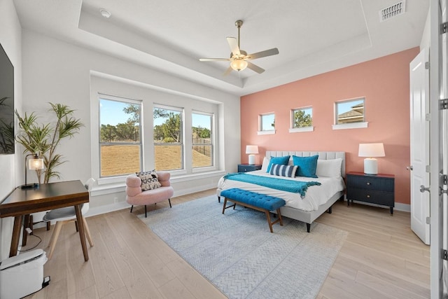 bedroom with a tray ceiling, light wood-style flooring, baseboards, and visible vents