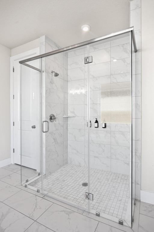 full bath with baseboards, marble finish floor, and a stall shower