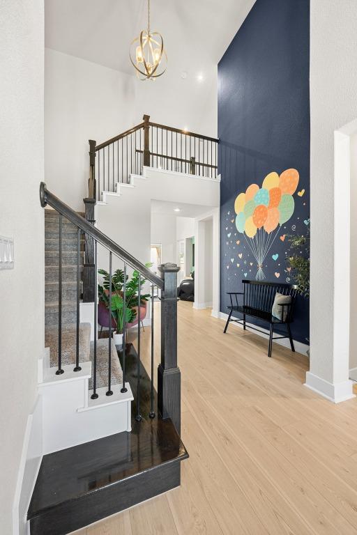 staircase with baseboards, a high ceiling, an inviting chandelier, and wood finished floors