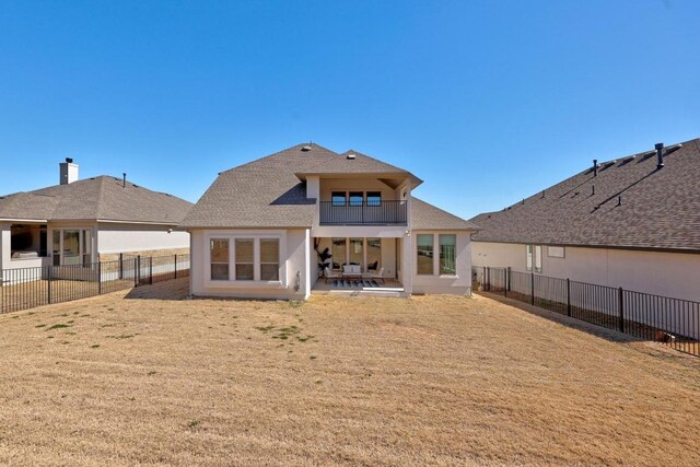 back of house featuring a balcony, a yard, a fenced backyard, a shingled roof, and a patio area