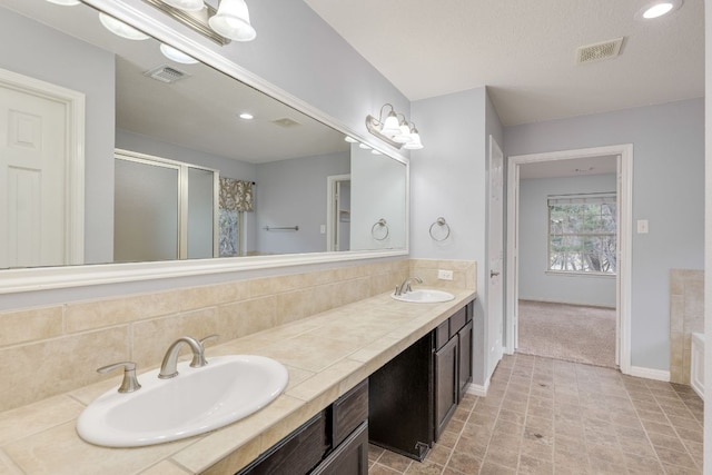 full bath with a sink, visible vents, a stall shower, and double vanity