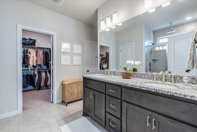 bathroom featuring baseboards, double vanity, a sink, a shower stall, and tile patterned floors