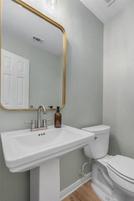 half bath featuring visible vents, baseboards, toilet, wood finished floors, and a sink