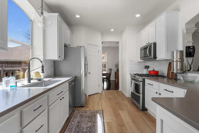 kitchen with tasteful backsplash, light wood-type flooring, white cabinets, stainless steel appliances, and a sink