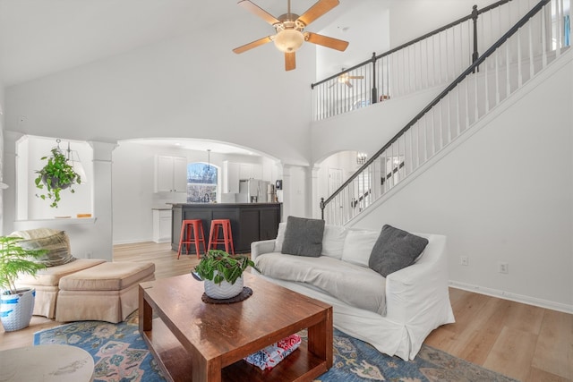 living area with a ceiling fan, stairway, arched walkways, light wood-style floors, and ornate columns