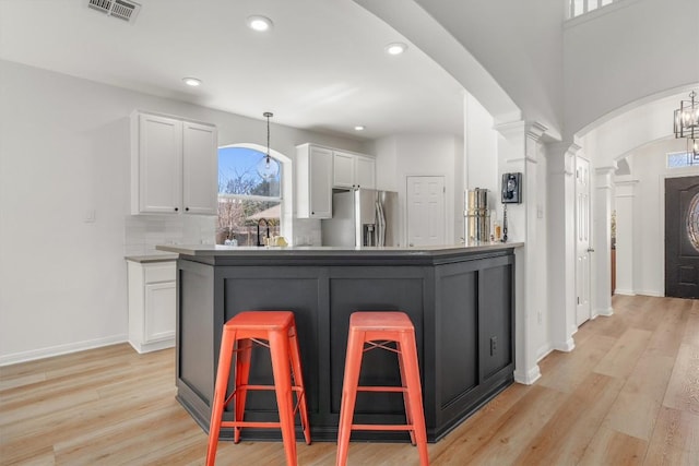 kitchen featuring visible vents, a breakfast bar area, stainless steel refrigerator with ice dispenser, and white cabinetry