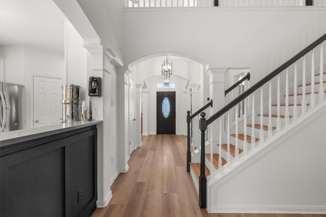 foyer entrance featuring stairs, decorative columns, a high ceiling, light wood-style floors, and arched walkways