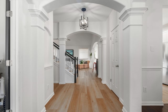 foyer entrance with light wood-style flooring, arched walkways, decorative columns, baseboards, and stairs