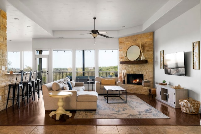 living room featuring a stone fireplace, a raised ceiling, wood finished floors, and ceiling fan