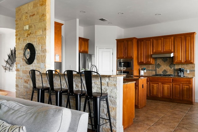 kitchen with visible vents, under cabinet range hood, tasteful backsplash, appliances with stainless steel finishes, and a breakfast bar area