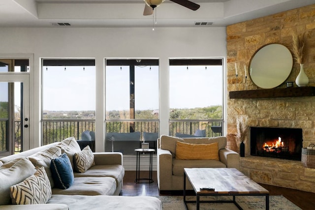 living area with visible vents, a stone fireplace, wood finished floors, and a ceiling fan