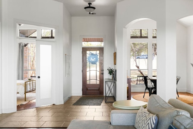 foyer with arched walkways, visible vents, and baseboards