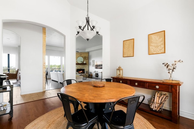 dining room featuring baseboards, a fireplace, an inviting chandelier, wood finished floors, and arched walkways