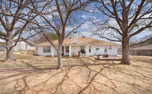 back of property featuring brick siding, a fire pit, a chimney, and fence