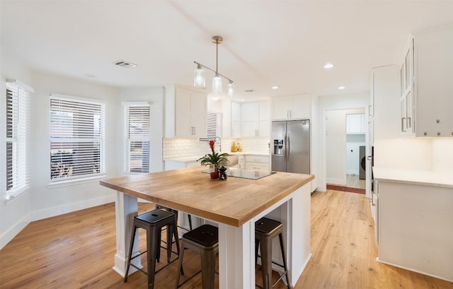 kitchen with visible vents, black electric stovetop, stainless steel refrigerator with ice dispenser, white cabinetry, and wood counters