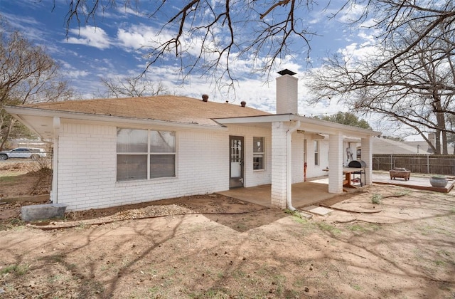 rear view of property with a patio, brick siding, a chimney, and fence