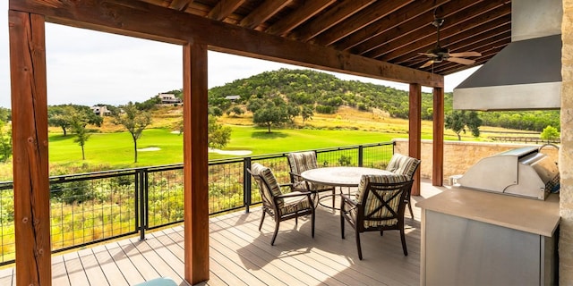 wooden deck featuring ceiling fan, view of golf course, a lawn, outdoor dining area, and area for grilling