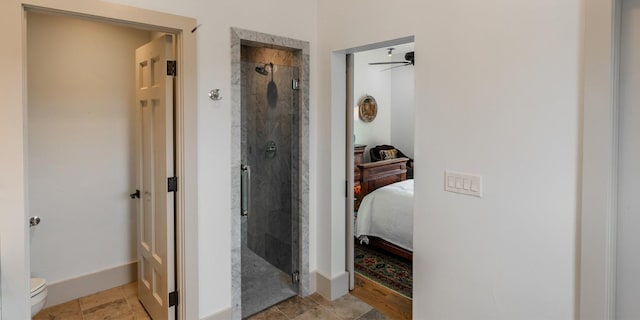 ensuite bathroom featuring connected bathroom, stone finish flooring, baseboards, toilet, and a stall shower