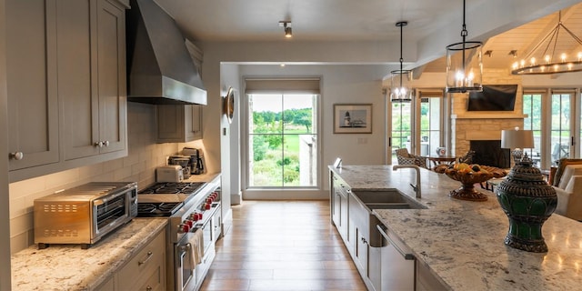 kitchen featuring backsplash, wall chimney range hood, light stone counters, light wood-style floors, and stainless steel appliances