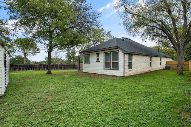 exterior space with stone siding, a fenced backyard, a yard, a shingled roof, and central AC unit