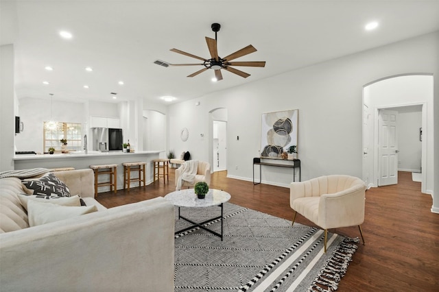 living area featuring arched walkways, recessed lighting, dark wood-type flooring, and a ceiling fan