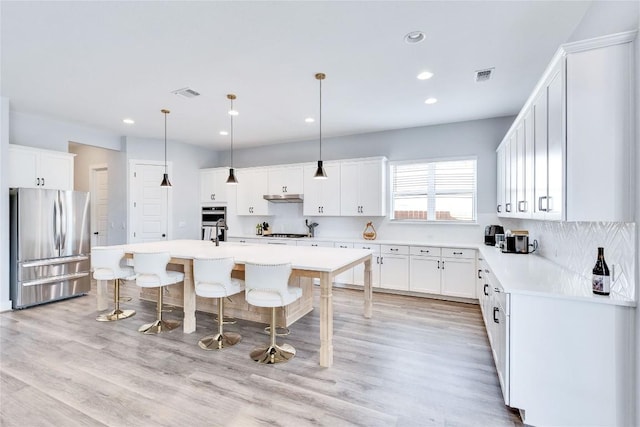 kitchen featuring visible vents, under cabinet range hood, an island with sink, a kitchen bar, and appliances with stainless steel finishes