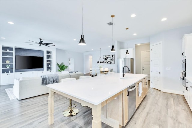 kitchen featuring light wood-type flooring, recessed lighting, stainless steel appliances, white cabinetry, and a kitchen island with sink